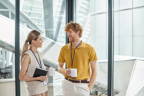 Dos compañeros de trabajo felices en ropa inteligente sonriendo y hablando entre sí, mientras que en el descanso del café, coworking - foto de stock