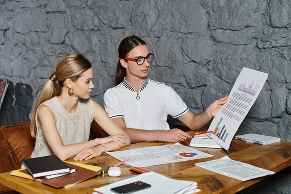 Dos jóvenes colegas en la mesa trabajando duro en su papeleo mirando gráficos, concepto de coworking - foto de stock