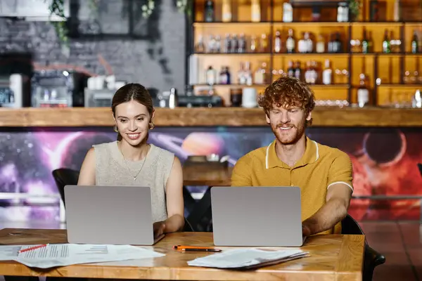 Two cheerful colleagues smiling while working on laptops with blurred bar on backdrop, coworking — Stock Photo