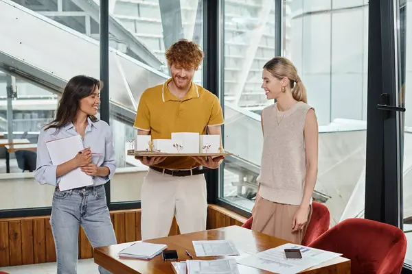 Drei fröhliche junge Teammitglieder lächeln und betrachten das maßstabsgetreue Modell des Gebäudes, Designbüro — Stockfoto