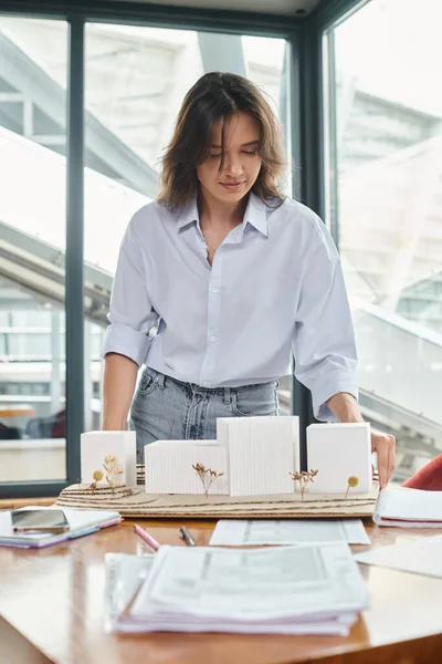 Jeune femme brune travaillant sur ses documents et maquette avec verre sur toile de fond, bureau de design — Photo de stock