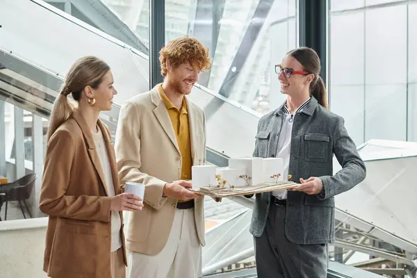 Three cheerful coworkers holding scale model and tea cup while doing their job, design bureau — Stock Photo