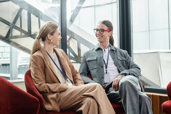 Dois colegas elegantes em desgaste inteligente sentados em cadeiras vermelhas e olhando um para o outro, co-trabalhando — Fotografia de Stock