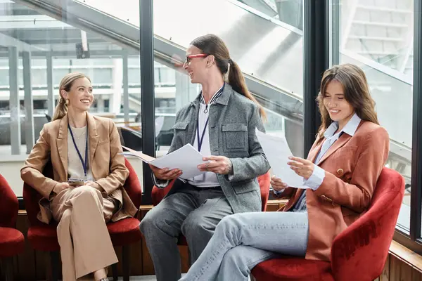Drei gut gelaunte Teammitglieder sitzen auf roten Stühlen und diskutieren Papierkram, Coworking-Konzept — Stockfoto