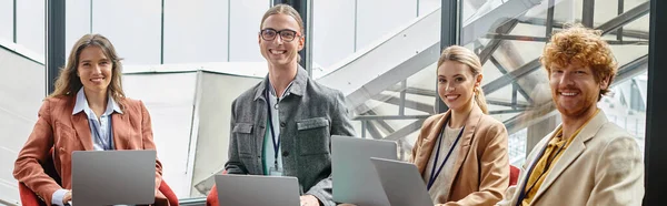 Cheerful young team in smart casual wear holding laptops and looking at camera, coworking, banner — Stock Photo