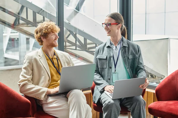 Young smiley colleagues working together on their laptops and looking at each other, coworking — Stock Photo