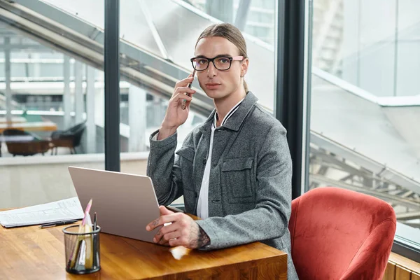 Young handsome worker looking at camera while working and talking on phone, coworking concept — Stock Photo