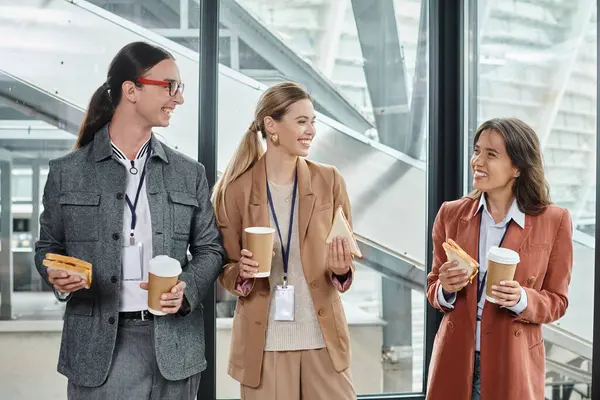 Tre colleghi che fanno pausa pranzo sorridendo sinceramente e mangiando panini, concetto di coworking — Foto stock