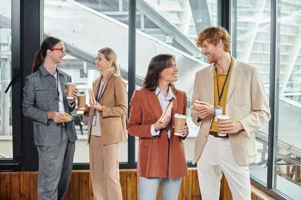 Quattro colleghi creativi che fanno pausa pranzo degustazione panini e caffè, concetto di coworking — Foto stock