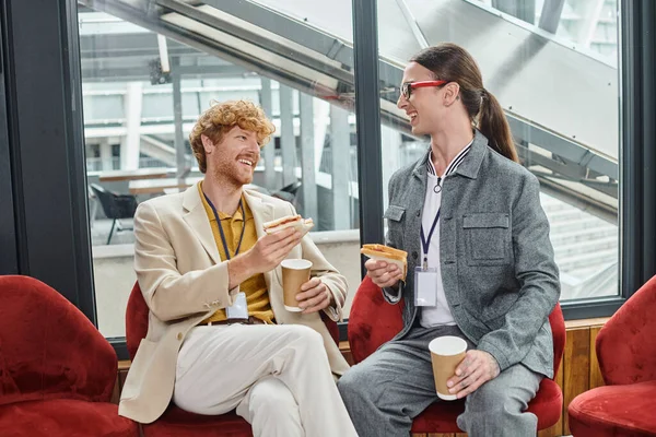 Due giovani colleghi maschi in pausa pranzo parlando e gustando caffè con panini, coworking — Foto stock