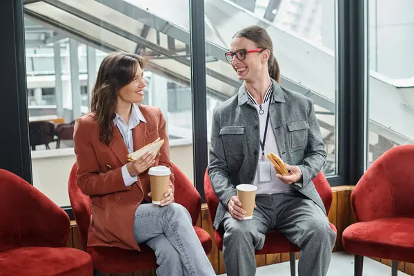 Dois colegas de trabalho em trajes casuais inteligentes sentados em cadeiras conversando e comendo, conceito de coworking — Fotografia de Stock