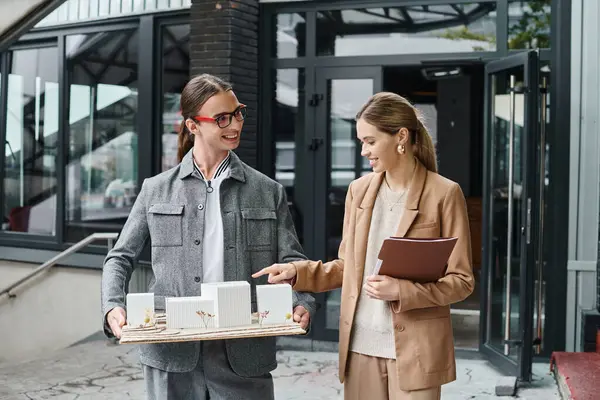Two smiley colleagues discussing scale model holding papers and smiling sincerely, design bureau — Stock Photo