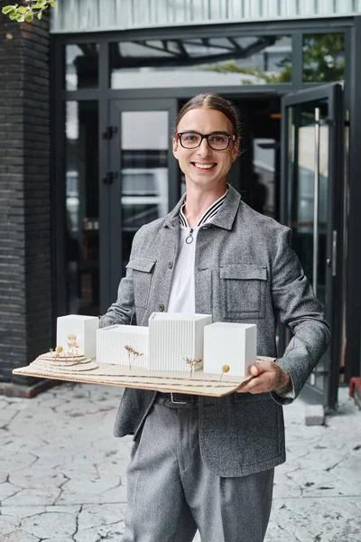 Jovem homem alegre em óculos com escala modelo de edifício olhando para a câmera, escritório de design — Fotografia de Stock