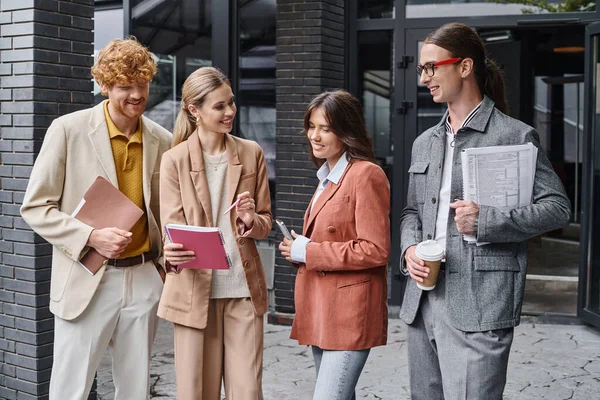 Four colleagues discussing their paperwork outdoors holding mobile phone and coffee cup, coworking — Stock Photo
