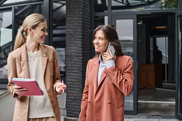 Young female coworkers standing outside holding papers and talking on phone, coworking concept — Stock Photo