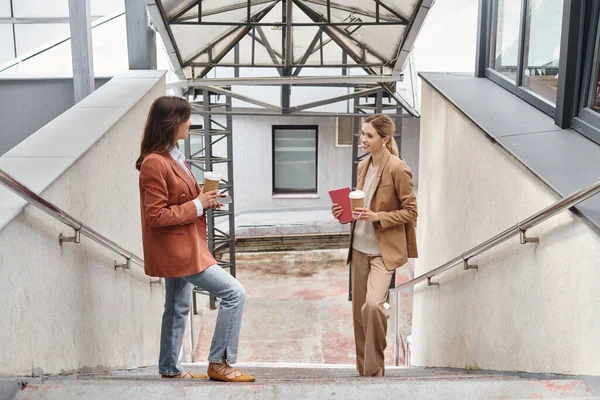 Two colleagues in business casual attire standing on stairs smiling at each other, coworking concept — Stock Photo