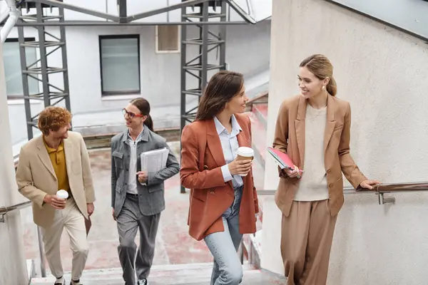 Quatro colegas alegres andando lá em cima segurando sua papelada e xícaras de café, conceito de coworking — Fotografia de Stock