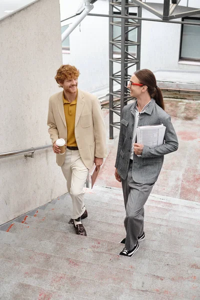 Dos colegas varones jóvenes caminando arriba hablando y sonriendo el uno al otro, concepto de coworking - foto de stock