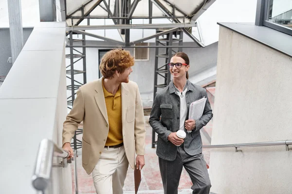 Compañeros de trabajo alegres hablando entre sí y sosteniendo sus papeles de trabajo, concepto de coworking - foto de stock