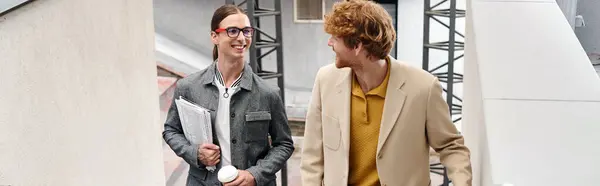 Two young coworkers talking to each other and holding their papers and coffee, coworking, banner — Stock Photo