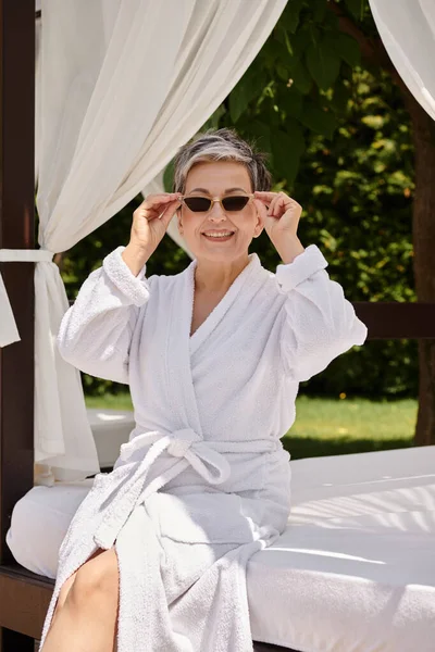 Glückliche Frau mittleren Alters mit Sonnenbrille, die sich während des Wellness-Rückzugs im privaten Strandpavillon ausruht — Stockfoto