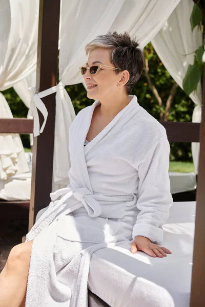 Весела жінка середнього віку в сонцезахисних окулярах відпочиває в приватному пляжному павільйоні під час оздоровчого відступу — стокове фото
