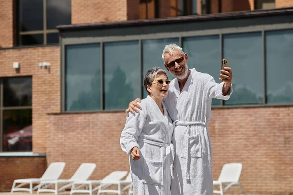 Glückliches Paar mittleren Alters in Roben, die Selfie auf dem Smartphone in Luxus-Resort, Wellness-Rückzugsort — Stockfoto