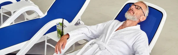 Wellness concept, mature man in glasses and robe resting on lounger near cocktail in spa, banner — Stock Photo
