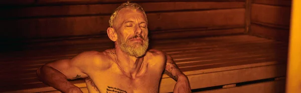Homme d'âge moyen tranquille, détendu et torse nu avec tatouages assis dans le sauna, bien-être, bannière — Photo de stock
