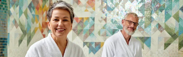 Glückliches Paar mittleren Alters in weißen Roben, die zusammen in Marmorsauna, Wellness-Spa, Banner sitzen — Stockfoto