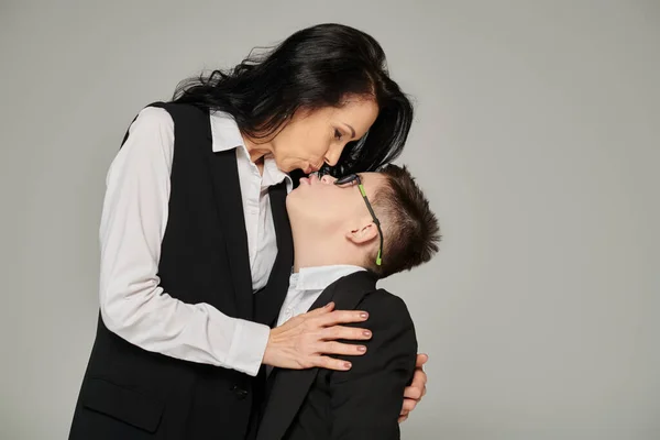 Mujer en formal desgaste besar hijo con abajo síndrome en uniforme escolar en gris, amor incondicional - foto de stock