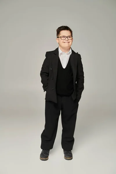 Schoolboy with mental disability posing in black suit with hands in pockets on grey — Stock Photo