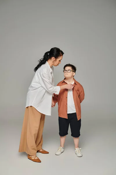 Middle aged woman talking to son with down syndrome in eyeglasses on grey, supportive parent — Stock Photo