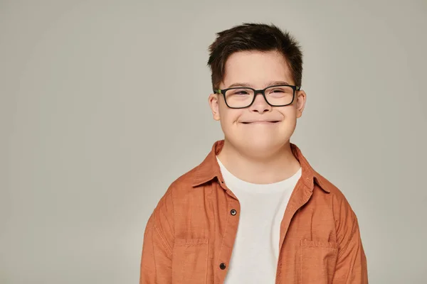 Портрет радостного мальчика с умственной отсталостью, в рубашке и очках, улыбающегося на сером — стоковое фото