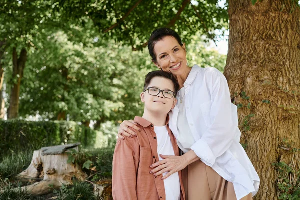 Happy middle aged woman embracing son with down syndrome while standing in park — Stock Photo