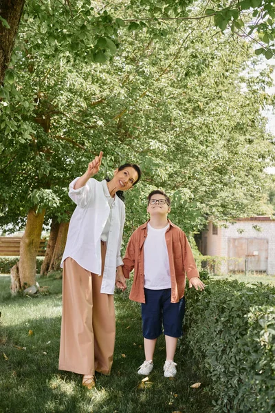 Middle aged woman pointing with finger during park outing with joyful son with down syndrome — Stock Photo
