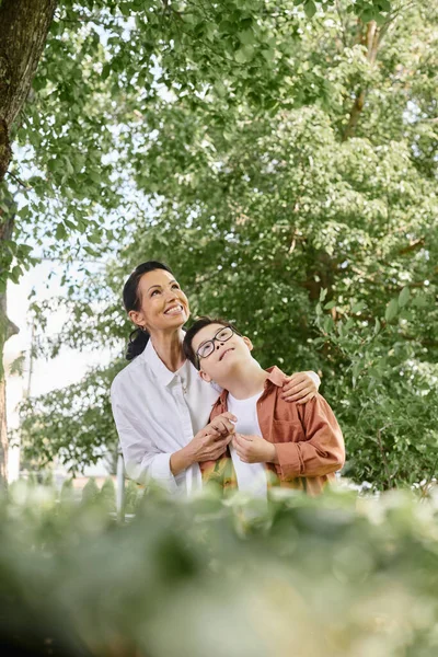 Весела жінка середнього віку і син з синдромом вниз дивиться на розмитий передній план в парку — стокове фото