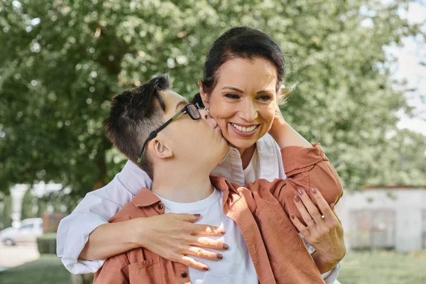 Kid with down syndrome kissing smiling middle aged mother during park outing, happy moments — Stock Photo