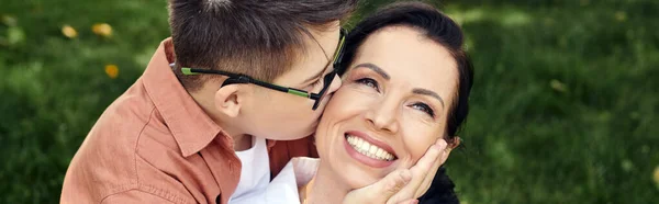 Kid with down syndrome, in eyeglasses, kissing happy mother in park, emotional connection, banner — Stock Photo