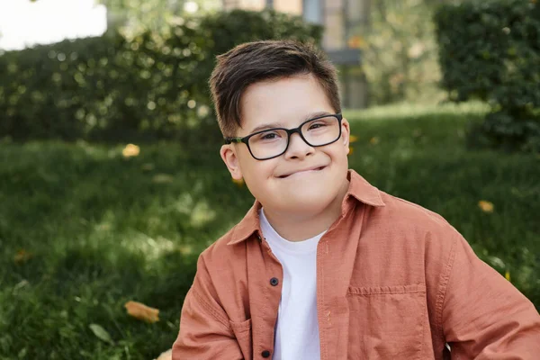Portrait of carefree boy with down syndrome, in eyeglasses, with genuine smile in park — Stock Photo