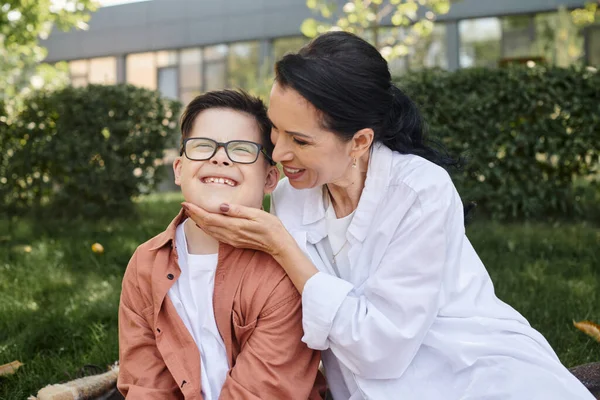 Счастливая женщина средних лет трогает лицо сына с синдромом Дауна в парке, безусловная любовь — стоковое фото