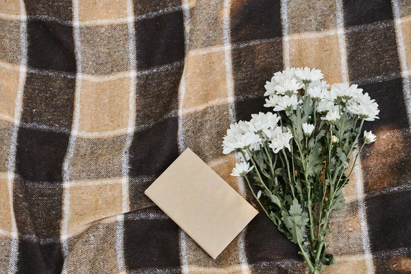 Top view of book and white chrysanthemums on plaid picnic blanket, quality time concept — Stock Photo