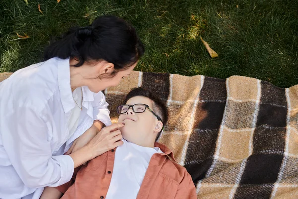 Vista dall'alto di donna che tocca la faccia di figlio con sindrome giù su coperta in parco, amore e cura — Foto stock