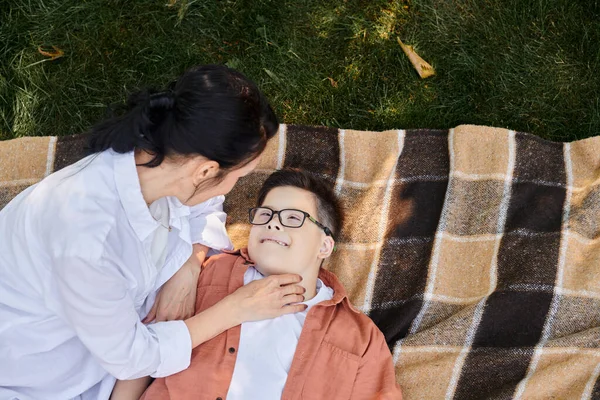 Visão superior de mãe perto de filho feliz com síndrome de baixo em cobertor no parque, amor incondicional — Fotografia de Stock