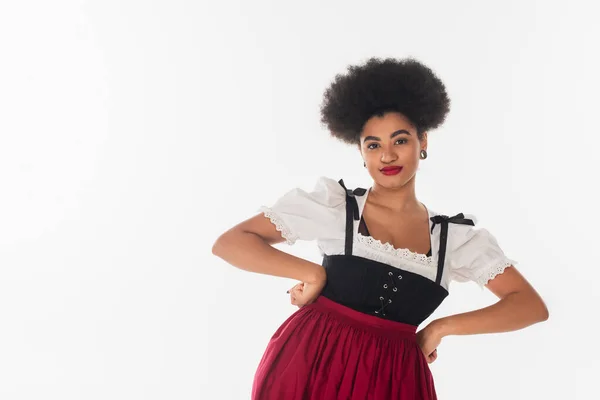 Confident african american oktoberfest waitress in traditional attire with hands on hips on white — Stock Photo