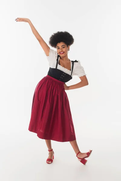 Emocionado africano americano oktoberfest camarera posando en bavarian dirndl en blanco, longitud completa - foto de stock