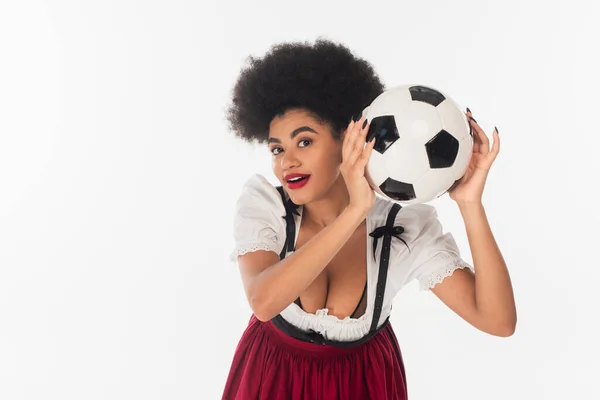 Eccitata cameriera afroamericana oktoberfest con pallone da calcio guardando la macchina fotografica su bianco — Foto stock