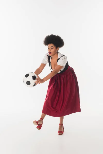 Africano americano oktoberfest camarera en tradicional bavarian dirndl jugando fútbol en blanco - foto de stock