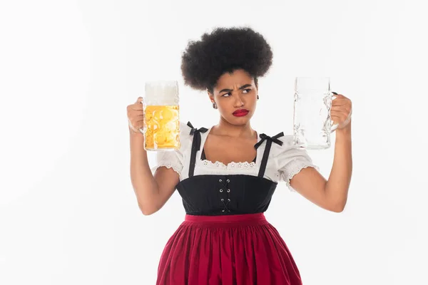 Descontento africano americano oktoberfest camarera en dirndl mirando taza de cerveza vacía en blanco - foto de stock