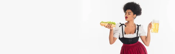 Heureux serveuse bavaroise afro-américaine avec tasse et hot dog sur blanc, oktoberfest, bannière — Photo de stock